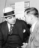Capone in a dark grey three piece suit and fedora